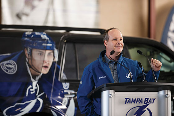 Steve Griggs speaking at a podium with a Tampa Bay Lightning vehicle behind