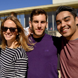 three alumni friends smiling at camera on campus